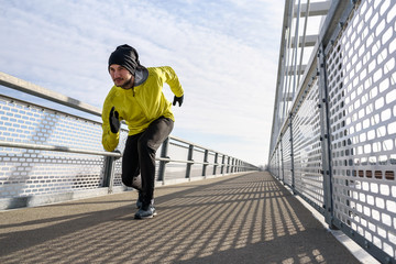 Attractive fit man running fast along big modern bridge. Exercising, Jogging, Sport, Winter. Male athlete running.