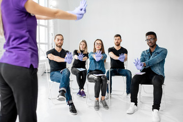 Group of young people sitting and listening to the instructor showing how to keep hands during the first aid artificially breathing indoors