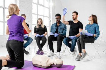 Group of young people sitting and listening to the instructor showing some practise with medic dummy during the first aid training indoors