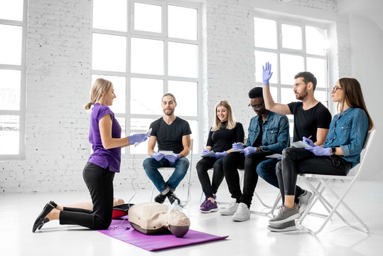 Group of young people sitting and listening to the instructor showing some practise with medic dummy during the first aid training indoors