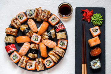 sushi rolls Asian food on round slate black Board with wasabi and ginger, soy sauce on white...