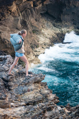 A girl stands on the edge of a cliff near the ocean in a strong wind.