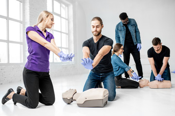 Group of young people practising to make artificial breathing with medical dummies during the first aid training in the white room