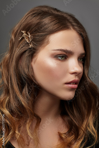 Close up portrait of a young brunette lady with natural make,up and wavy hairstyle. Her tresses are adorned with bronze twig hair clip.