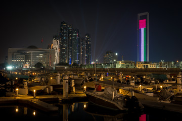 Beautiful view of Abu Dhabi city famous landscape displaying UAE flag, Etihad towers and Marina boats at night