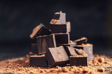 Pieces of dark bitter chocolate with cocoa powder on dark wooden background. Concept of...