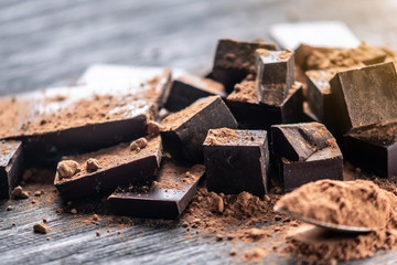 Pieces of dark bitter chocolate with cocoa powder on dark wooden background. Concept of...