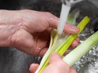 Männerhände wäscht Lauchstangen unter fließendem Wasser in einem Küchenbecken