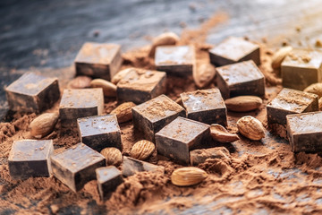 Pieces of dark bitter chocolate with cocoa and almonds nuts on wooden background. Card with space...