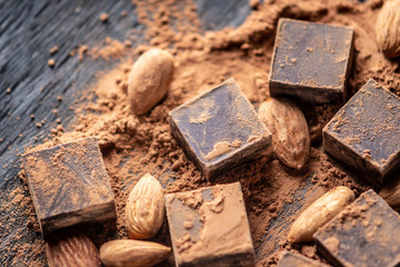 Pieces of dark bitter chocolate with cocoa and almonds nuts on wooden background. Card with space for text