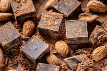 Pieces of dark bitter chocolate with cocoa and almonds nuts on wooden background. Card with space for text