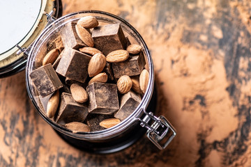 Pieces of dark bitter chocolate with cocoa and nuts almonds on wooden background. Concept of confectionery ingredients