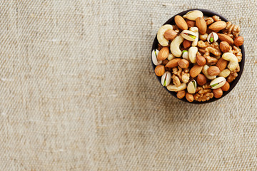 Mix of different nuts in a wooden cup against the background of fabric from burlap. Nuts as structure and background, macro. Top view.
