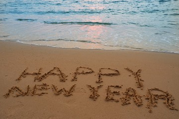 Happy new year concept handwriting on the sand beach.