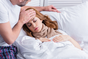 Fototapeta na wymiar husband touching forehead of sick wife with fever in bed