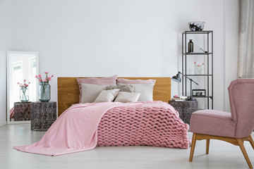 Pink cozy woolen blanket and duvet on comfortable king size bed in fashionable bedroom interior