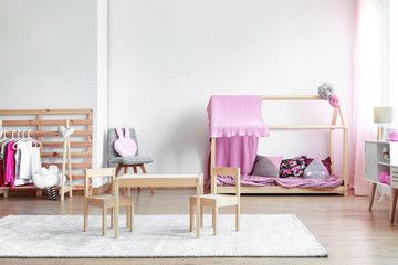 Copy space on empty white wall in cute pink and wooden girly bedroom with toys, clothes and scandinavian bed