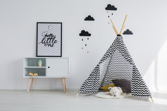 Patterned black and white scandinavian tent with grey and yellow pillows and white teddy bear next to wooden cabinet