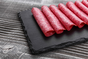 delicious sliced salami on a stone plate wooden background