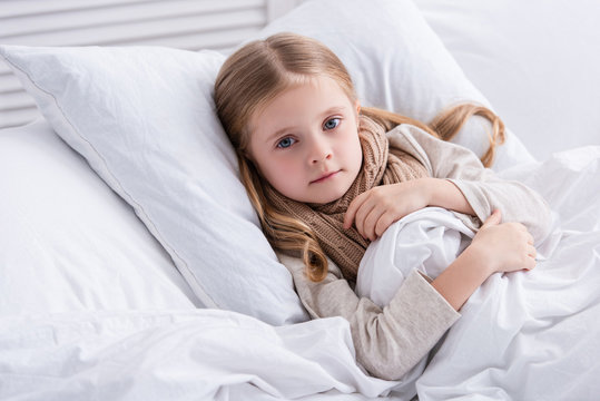 sick child with scarf over neck lying in bed at home and looking at camera