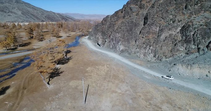 4k 60 fps Mongolia Aerial view of Altai desrt track with 4x4 driving - flying over pine tree small forest close to rocky mountain