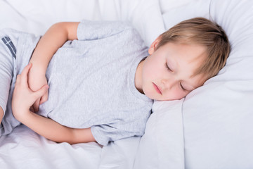 sick boy lying on bed and touching painful stomach in bedroom