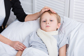 cropped image of mother taking care of sick son and touching his forehead in bedroom