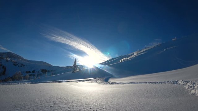 the snowboarder rolls down the ridge down the snowy mountain valley and makes a beautiful turn with a trail of snow splashes. front view in front of the sun. white snow and blue sky. 4k super quality