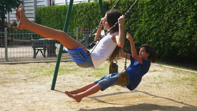 boy and girl teenager swinging on a swing with bare feet on the green lawn of the backyard of his house