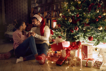 young couple next to decorated Christmas tree, exchanging Christmas presents and having fun..