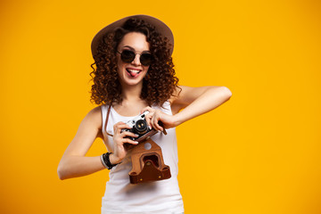 Portrait of laughing young woman in eyeglasses taking pictures on retro vintage photo camera isolated on bright yellow background. People sincere emotions, lifestyle concept. Advertising area.