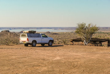 Landscape of the Kalahari desert with a roof tent 4x4 off-road veichle in Namibia, Africa - obrazy, fototapety, plakaty