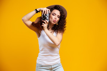 Obraz premium Portrait of laughing young woman taking pictures on retro vintage photo camera isolated on bright yellow background. People sincere emotions, lifestyle concept. Advertising area.