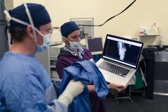 Female nurse showing x-ray report to male surgeon on laptop