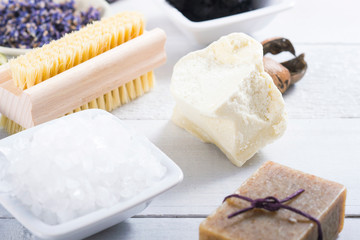 spa products: black mud and clay powder, cosmetic cream, soap, bath salt, shea butter and lavenders on white wood table background