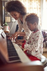 African American mother with child girl on Christmas play music on piano. concept of holidays and family happiness..