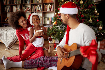 family sitting on floor together and listening guitar songs at home on Christmas.