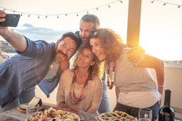souvenir photo with friends, evening on the beach, terrace with sunset behind, selfie with cell phone, happy and carefree friends, summer evening parties, beach holidays, smiles and photographs