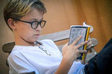 Young man intent on reading in the garden. Blond child reading his favorite book absorbed. Healthy pastime. Blondie on the bench reading an adventure book.