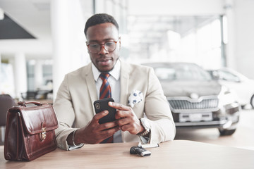 Attractive black businessman sits at the table at the car dealership, he signs a contract and buys a new car