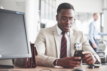 Attractive black businessman sits at the table at the car dealership, he signs a contract and buys a new car