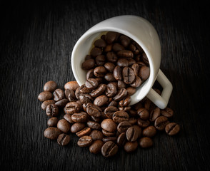 white Cup with coffee beans on dark wooden background close-up