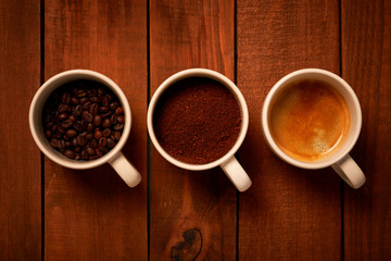 Three cups of espresso, freshly ground coffee and coffee beans on a wooden table from the top view