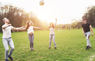 A group of friends in casual outfit play soccer in the open air. People have fun and have fun. Active rest and scenic sunset.