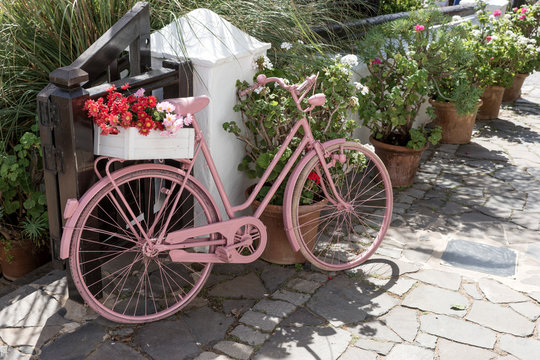 Pink bicycle with flowers on the walkway in front of the shop