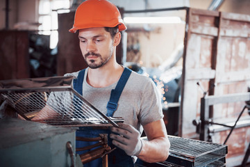 Portrait of a young worker in a hard hat at a large waste recycling factory. The engineer monitors...