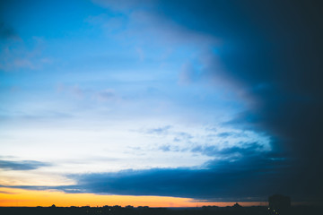 Cityscape with wonderful varicolored vivid dawn. Amazing dramatic blue cloudy sky above dark silhouettes of city buildings. Atmospheric background of orange sunrise in overcast weather. Copy space.