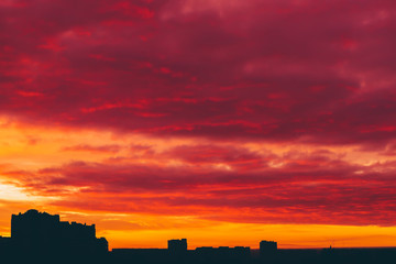 Cityscape with vivid surrealistic dawn. Amazing warm dramatic cloudy sky above dark silhouettes of...