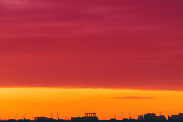 Cityscape with vivid surrealistic dawn. Amazing warm dramatic cloudy sky above dark silhouettes of city buildings. Orange sunlight. Atmospheric background of sunrise in overcast weather. Copy space.