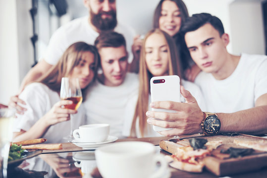 A group of people make a selfie photo in a cafe. The best friends gathered together at a dinner table eating pizza and singing various drinks